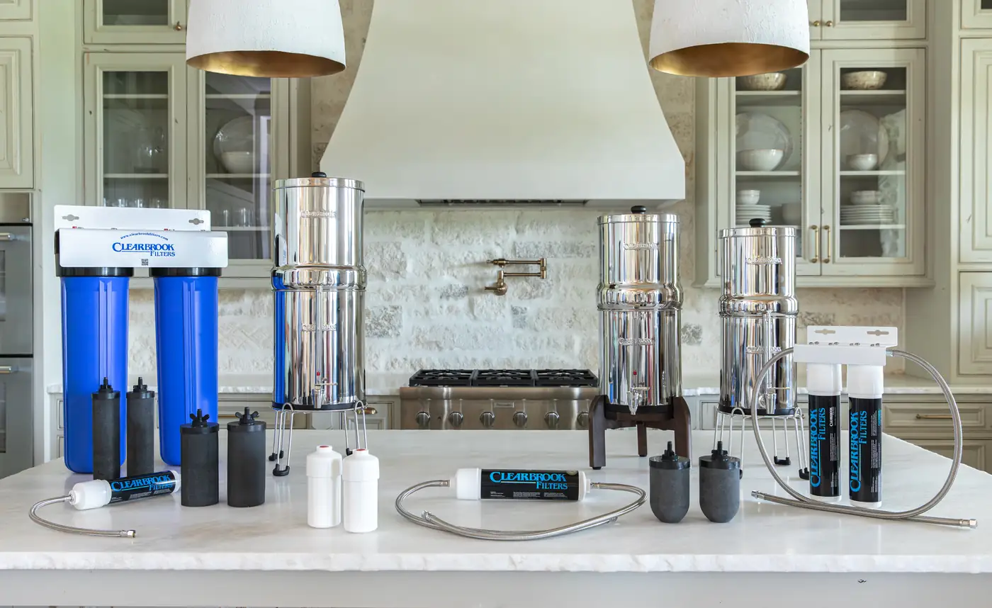The full Clearbrook range laid out on a kitchen island — under-sink dual housings, stainless gravity systems in several sizes, in-line filters, filter elements and connection hoses